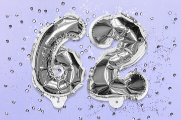 Silver foil balloon number, digit sixty two on a lilac background with sequins. Birthday greeting card with inscription 62. Anniversary concept. Top view. Numerical digit. Celebration event, template.