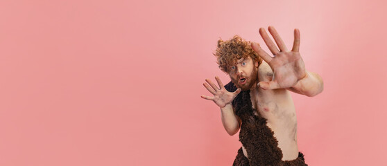 Cropped portrait of man in character of neandertal showing fear isolated over pink background. Flyer