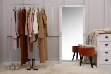 Fototapeta na wymiar Rack with different stylish clothes and shoes near grey wall in room