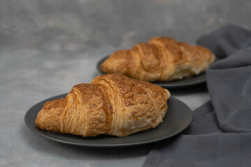 Freshly baked homemade croissants for breakfast. Traditional and whole-grain croissant in a gray plate on a concrete or stone background.
