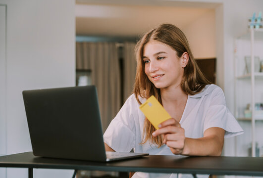 Female student holding credit card while using laptop at home