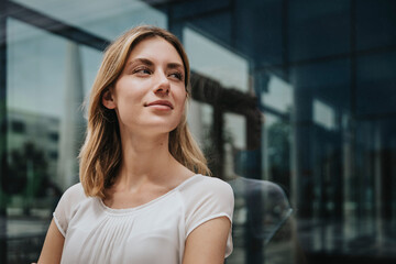 Blond woman looking away while day dreaming in front of glass wall