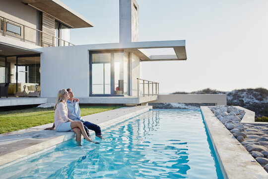 Relaxed couple sitting together at pool in backyard