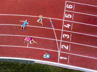 Germany, Baden Wurttemberg, Winterbach, Aerial view of three female sprinters resting on track right past finish line