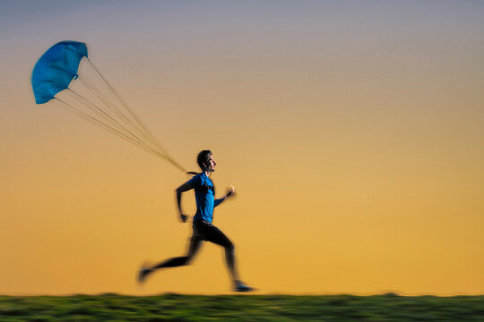 Male sportsperson jogging with parachute during sunset