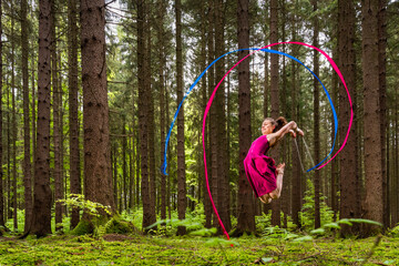 Young female gymnast practicing gymnastics with ribbons in forest