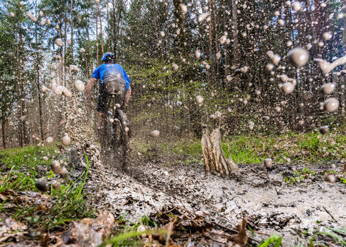 Young man riding mountain bike through mud in forest