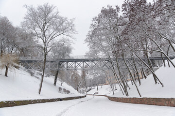 View of the snow-covered park in winter, snow-covered trees, bushes, and a bridge, Gomel, Belarus.