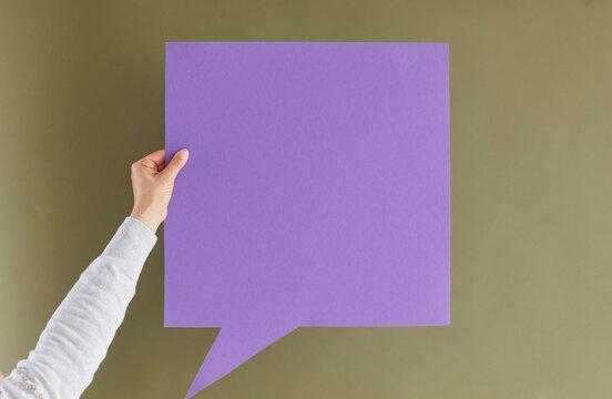 Express your thoughts. Unknown woman holding blank purple paper card in form of speech bubble on green khaki background. Concept of important messages, thoughts and ideas. Copy space.