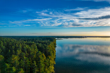 Aerial landscape of the lake and green forest in a sunny day. Blue sky, mirror image of clouds on the water. 