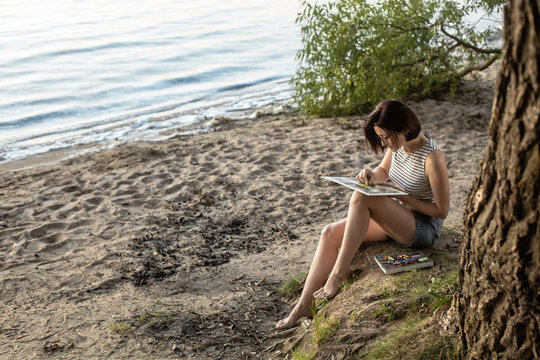 a girl draws on the shore in the evening
