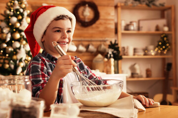 Cute little boy in Santa hat making dough for Christmas cookies at home