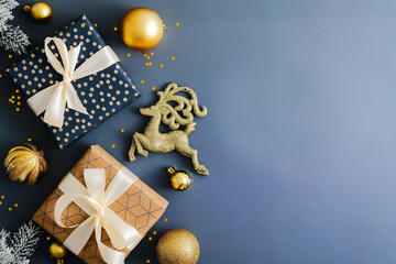Stylish Christmas background with gift boxes, gold baubles decoration and reindeer on dark blue...