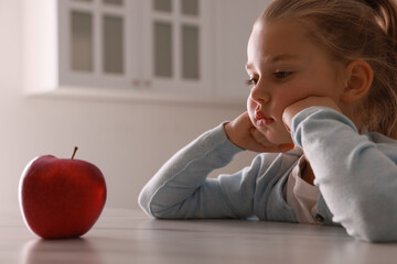 Cute little girl refusing to eat apple in kitchen
