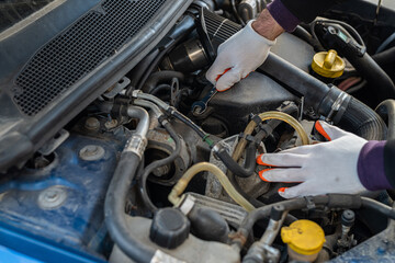 hands of a strong man mechanic in gloves repairs the car under the hood.