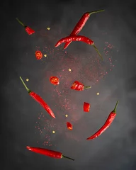 Poster Levitation or flying of red chili pepper whole and slices with paprika powder used for food seasoning to make hot spicy flavour in mexican and asian cuisine against dark black background. Vertical © Elena