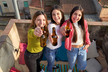 Cheerful female friends raising beer bottle while enjoying on rooftop