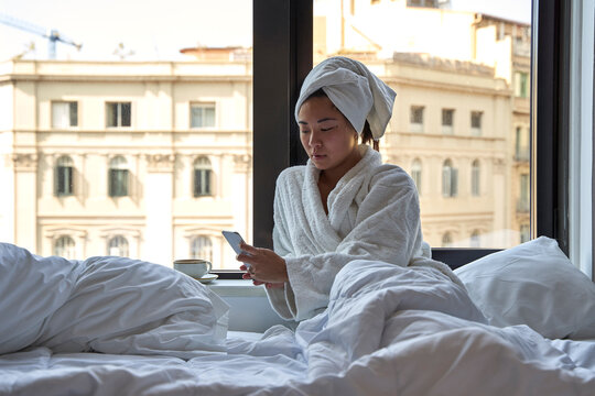Young woman using smart phone while sitting on bed of hotel