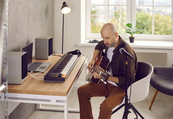 Focused serious male musician playing acoustic guitar creating new song in his home music studio....