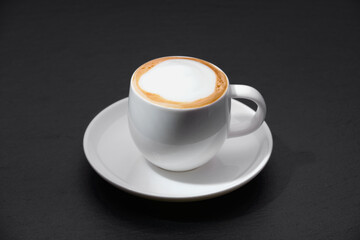 White cup of coffee on a black background. A cup of coffee on a textured black table.