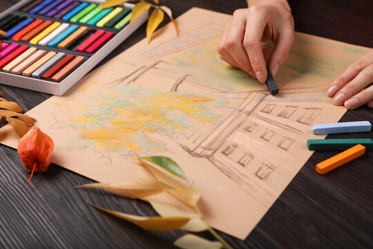 Woman drawing beautiful building with soft pastel at wooden table, closeup