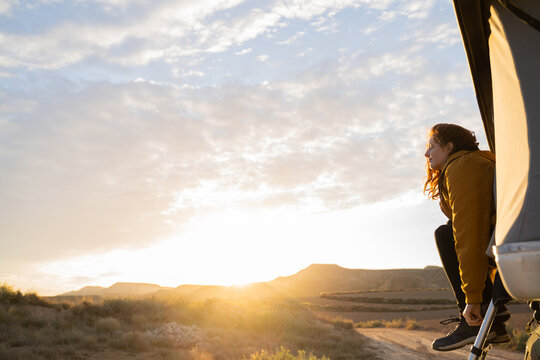 Woman sitting in camper van roof tent at sunrise