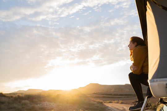 Woman sitting in camper van roof tent at sunrise