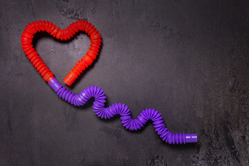 Tube toys bent as red heart balloon and wavy ribbon on black background