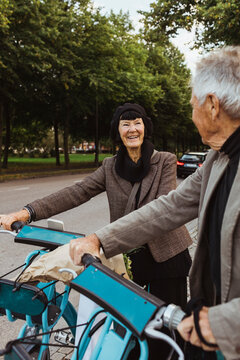 Smiling senior couple with electric bicycles on street