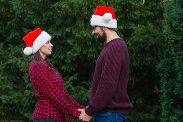 Young positive multi-ethnic couple in christmas santa hats celebrate Christmas tree outdoors copy