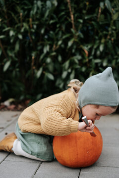 Little girl preparing to stab a pumpkin with a knife