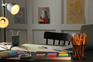 Artist's workplace with soft pastels, laptop and drawing pencils on table indoors