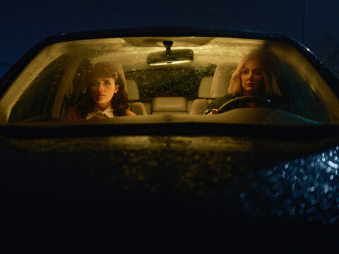 Two women sitting in a car at night looking concerned