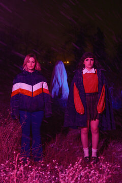 Two women stand oddly in field unaware of ghost