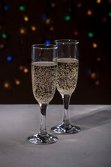 Champagne in two glasses. The concept of a festive New Year's Christmas card. Two glasses with sparkling wine against the background of multi-colored garland lights. Close-up, Selective focus, 