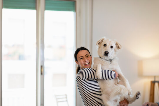 Cheerful female owner holding dog at home