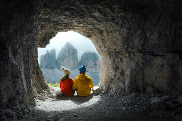 Couple of mountaineers observe the views of Tre Cime di Lavadero from inside a cave in the Italian Alps