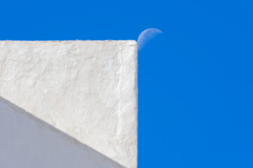 The moon next to a white facade.