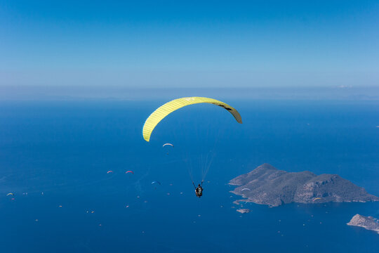 yellow paraglider flying over turquoise water