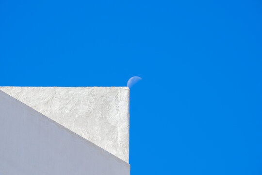 The moon next to a white facade.