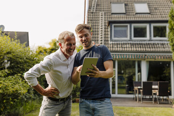 Son showing digital tablet to father in back yard