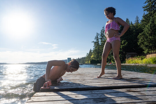 Girl in swimsuit watches boy pull himself onto dock