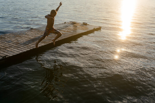 Boy leaps dramatically from dock into lake at sunset
