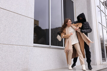 Woman fighting with thief while he trying to steal her bag near building, space for text. Self...