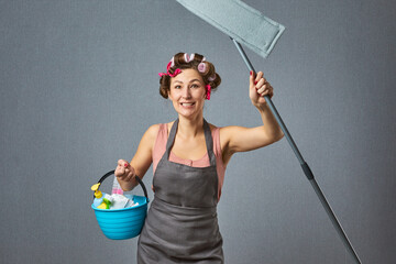 Positive wife hold bucket mop wear apron isolated pastel color background. Funny woman housewife dressed in retro style with Curler.
