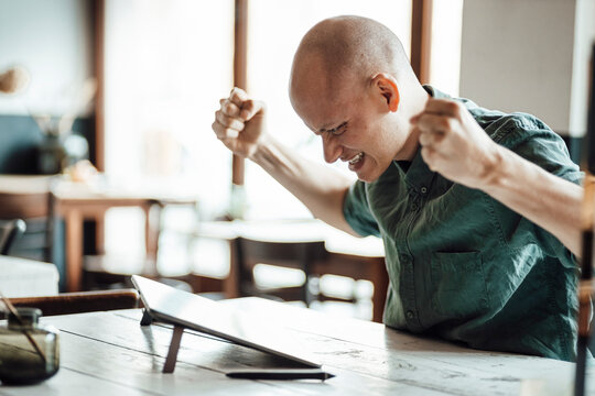 Bald male design professional cheering in excitement while looking at graphics tablet