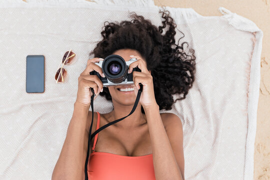 Smiling young woman photographing through camera while lying on towel at beach