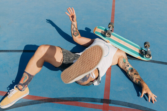 Fallen young man with skateboard on face at basketball court during sunny day