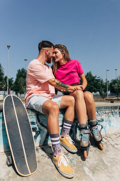 Young couple sitting face to face at skateboard park on sunny day