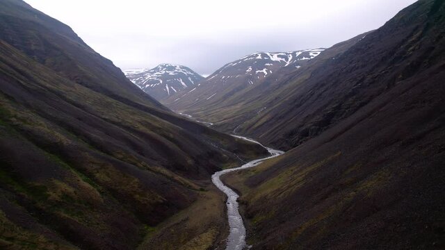 Aerial shot slowly rising above dramatic Icelandic mountain landscape. River flows below.